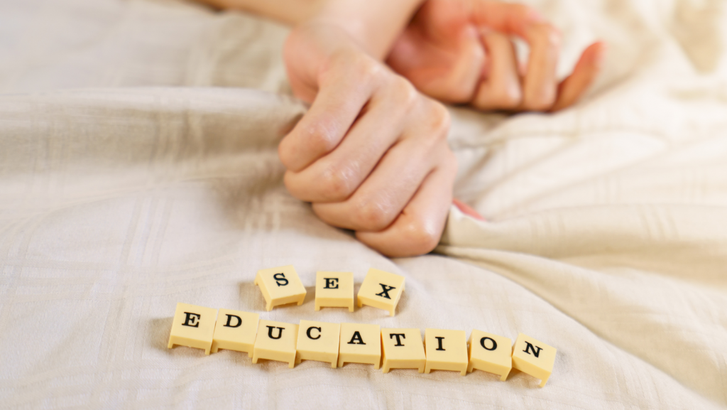 Two hands on a bed with scrabble text saying sex education